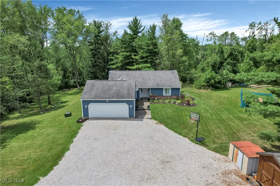 Ranch-style house with a shingled roof, an attached garage, an outbuilding, a front lawn, and gravel driveway