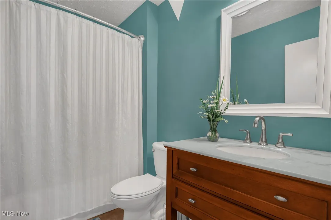 Bathroom with toilet, a shower with shower curtain, and vanity