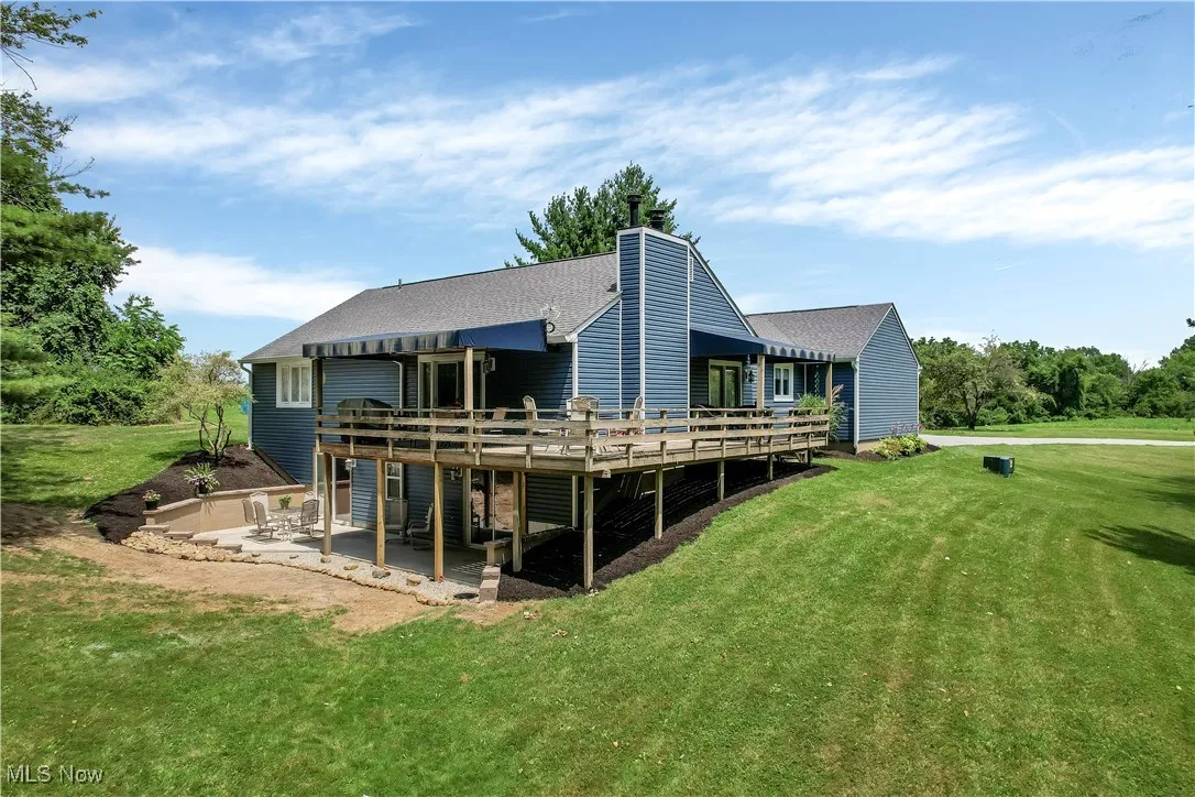 Rear view of house featuring a wooden deck, a lawn, a patio, roof with shingles, and a chimney