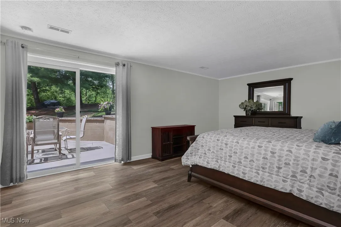 Bedroom featuring visible vents, access to exterior, a textured ceiling, and wood finished floors