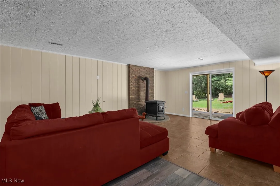 Living area featuring visible vents, a wood stove, a textured ceiling, wood finished floors, and wood walls