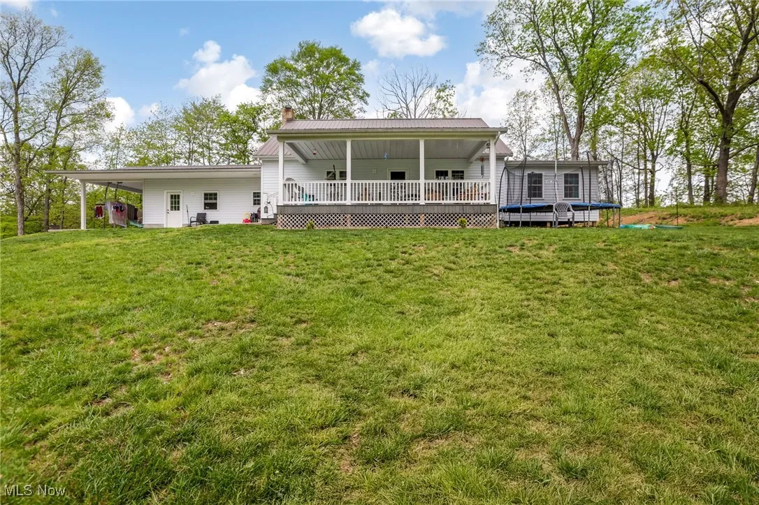 Rear view of house with a chimney, a yard, a trampoline, metal roof, and a deck