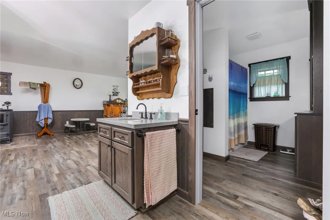 Kitchen with a sink, wood finished floors, open shelves, wainscoting, and dark brown cabinetry