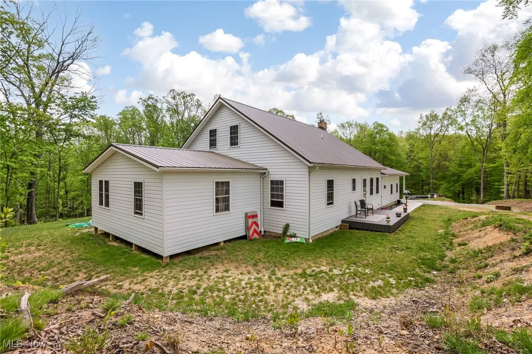 Back of property featuring a deck, metal roof, a yard, and a view of trees