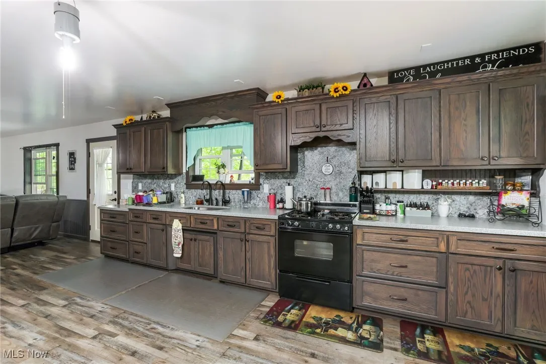 Kitchen with black range with gas cooktop, a sink, light countertops, wood finished floors, and backsplash