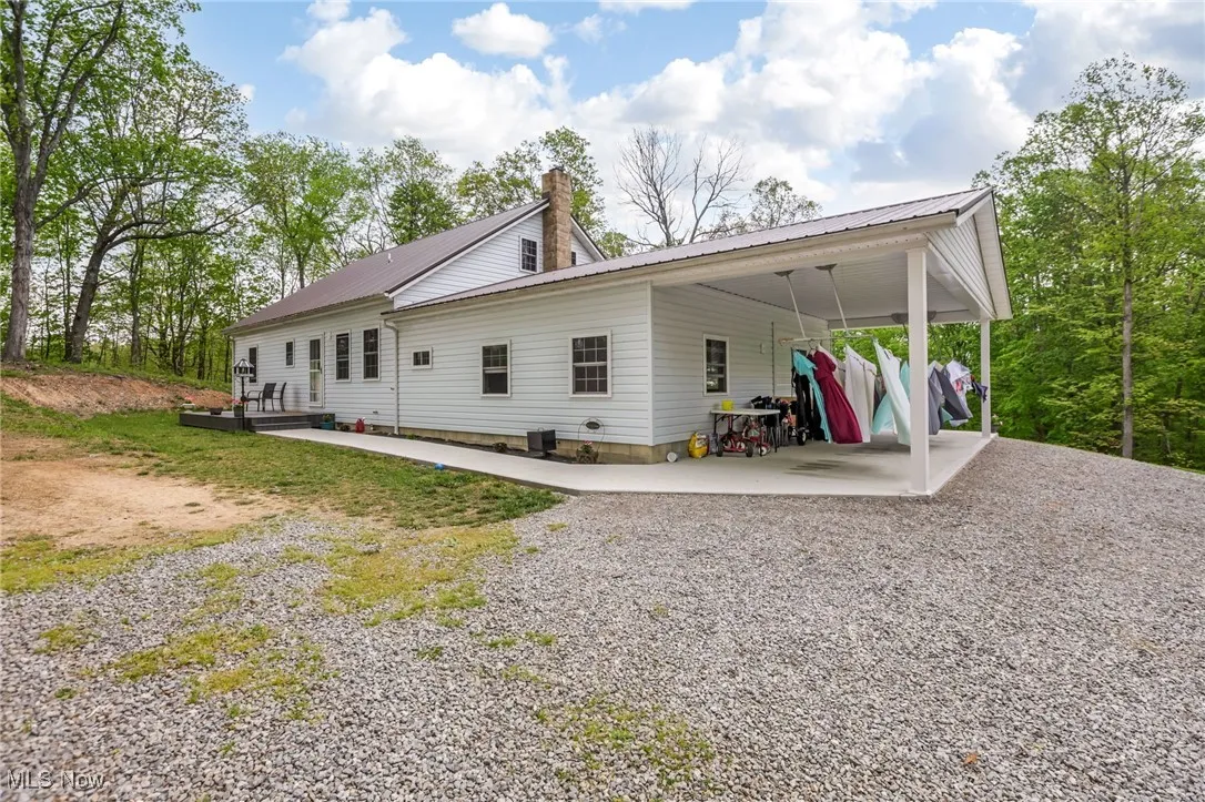 View of side of home featuring driveway, metal roof, a carport, and a chimney