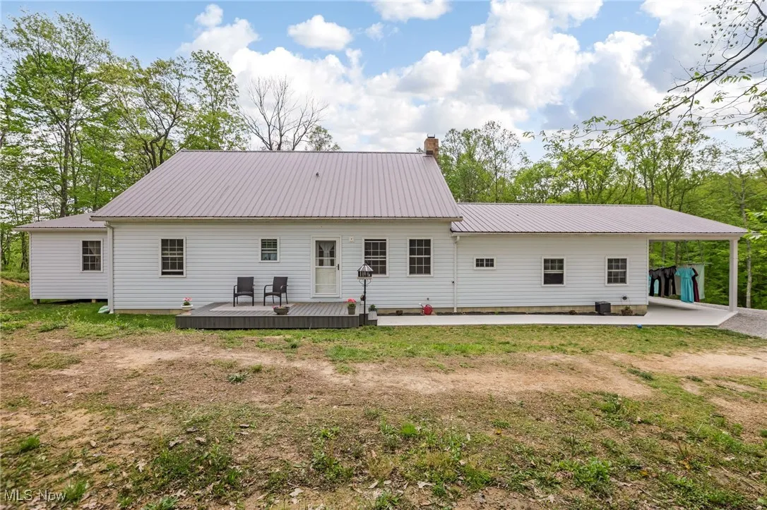 Rear view of property featuring a wooden deck, metal roof, a chimney, an attached carport, and a yard