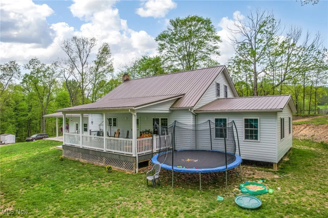 Back of property featuring a trampoline, a yard, metal roof, a chimney, and a wooden deck