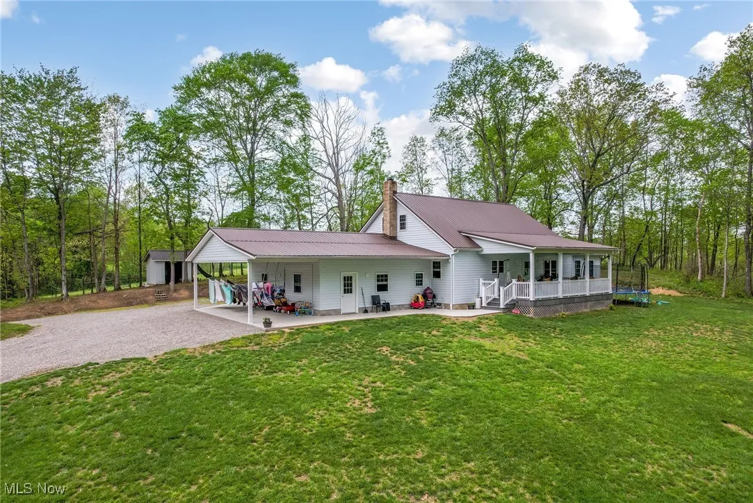 Rear view of property featuring gravel driveway, a lawn, a chimney, metal roof, and a carport
