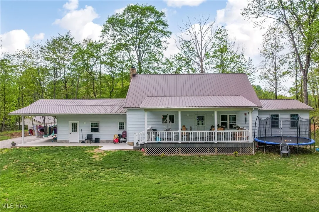 Back of property with a trampoline, a yard, a chimney, metal roof, and a patio area