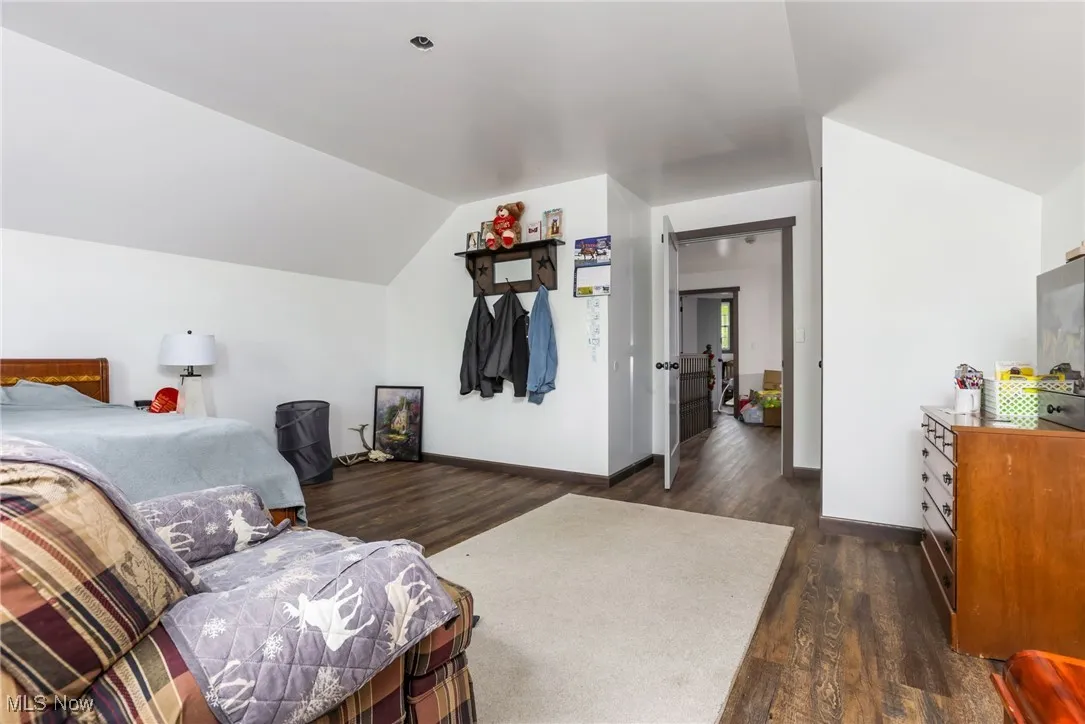 Bedroom with dark wood-style flooring, lofted ceiling, and baseboards