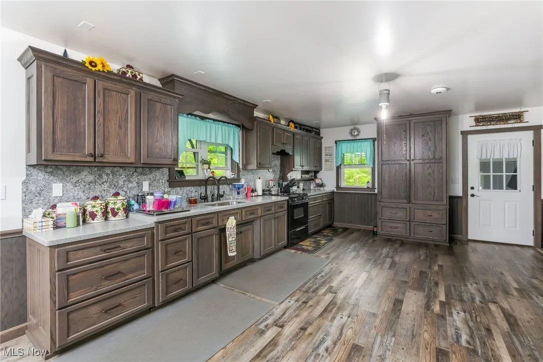 Kitchen with black range with gas stovetop, a sink, dark wood-style floors, light countertops, and tasteful backsplash