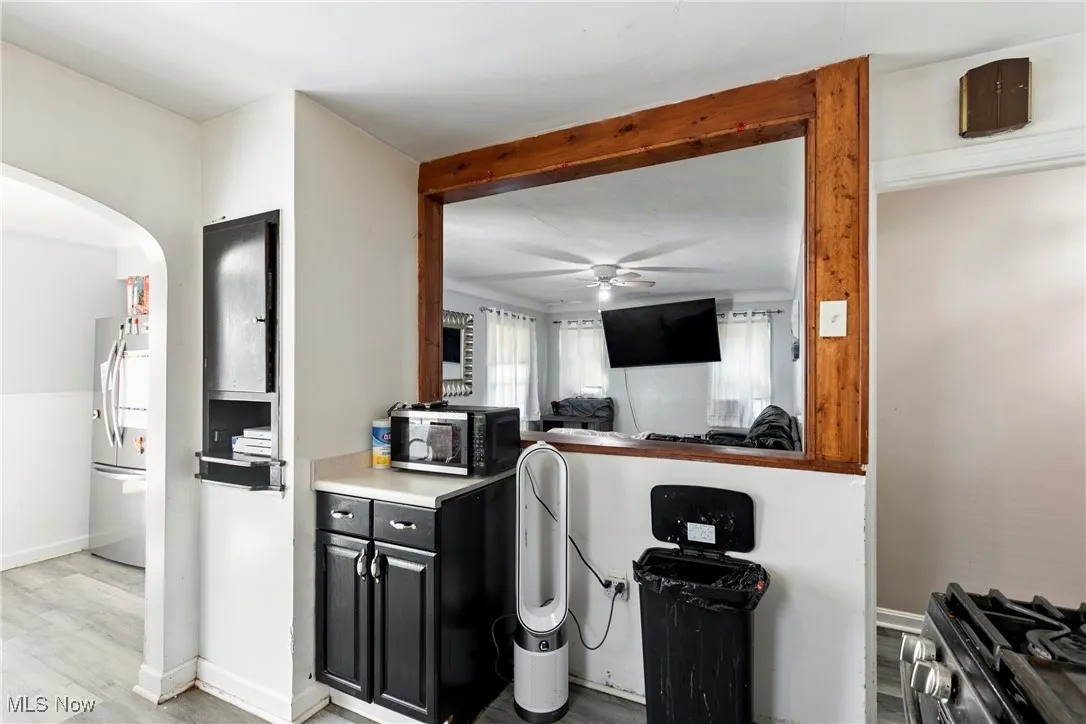 Kitchen with dark cabinetry, a ceiling fan, freestanding refrigerator, light wood-type flooring, and arched walkways