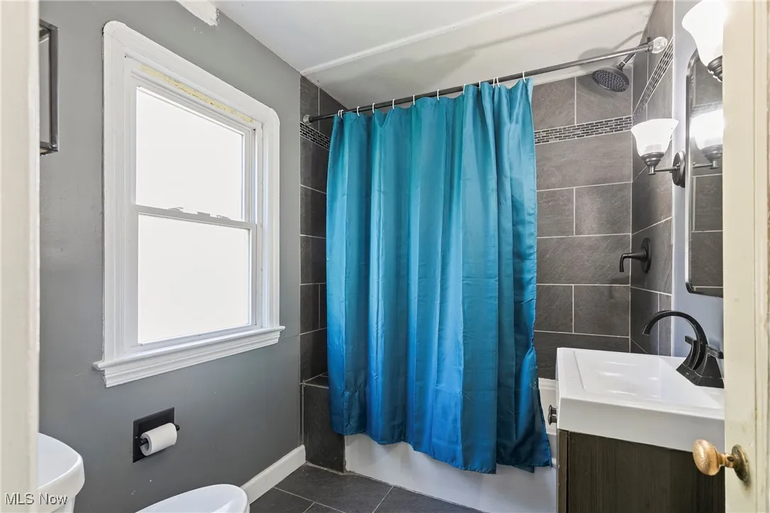 Bathroom featuring toilet, tile patterned floors, shower / bathtub combination with curtain, vanity, and baseboards