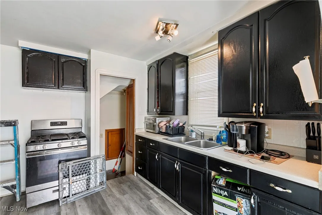 Kitchen featuring stainless steel gas range oven, dark cabinetry, a sink, and light countertops