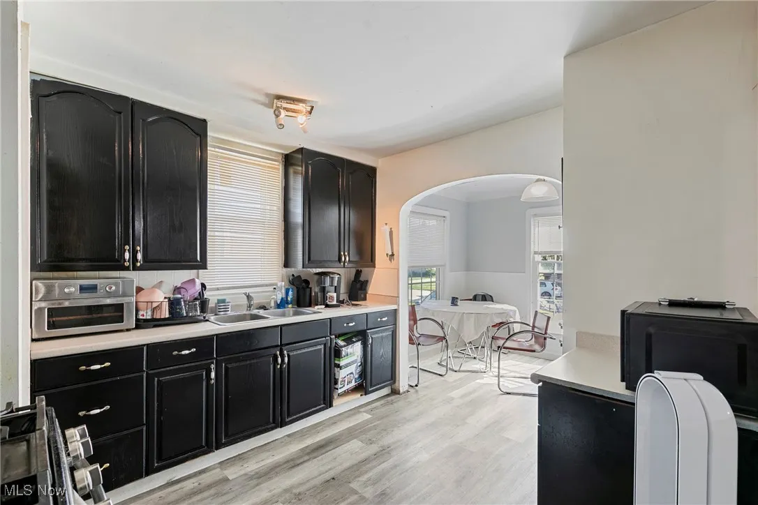 Kitchen featuring dark cabinets, a sink, arched walkways, light countertops, and light wood-type flooring