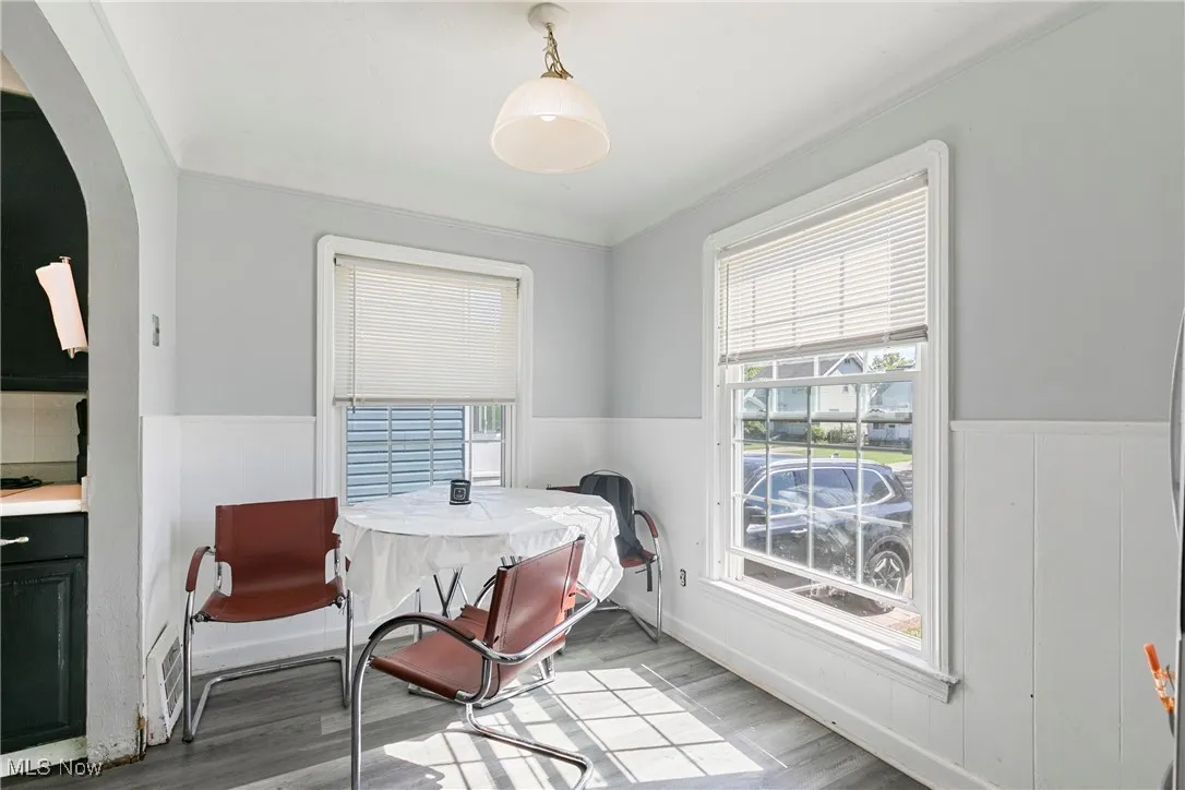 Dining room featuring arched walkways, wood finished floors, a wainscoted wall, and ornamental molding