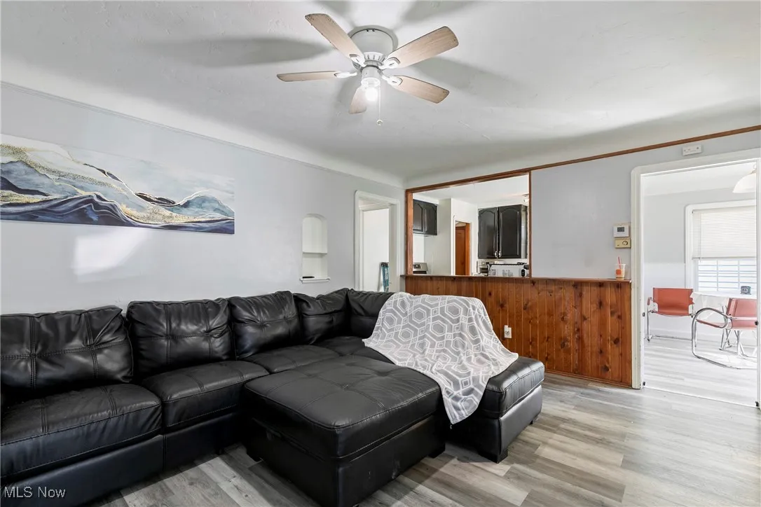 Living room with light wood finished floors, a wainscoted wall, and ceiling fan