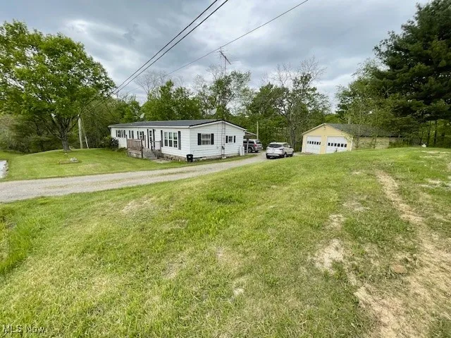 Manufactured / mobile home with a garage, a front lawn, and view of wooded area