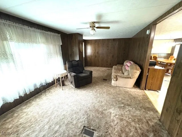 Sitting room featuring light colored carpet, wooden walls, and a ceiling fan