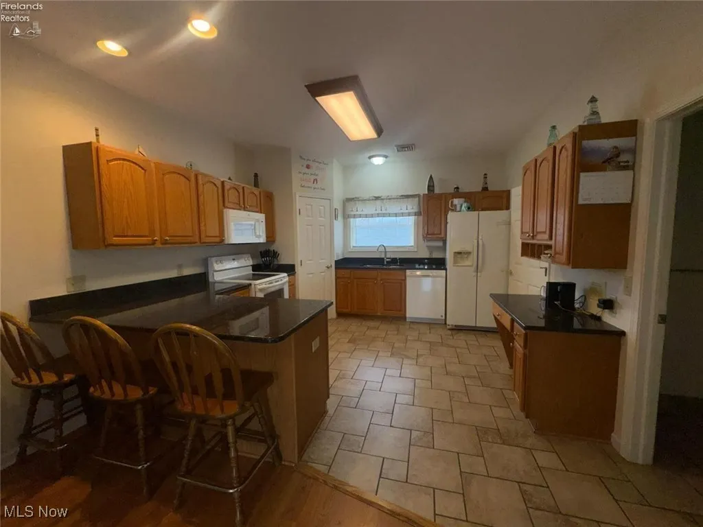 Kitchen featuring white appliances, a sink, a peninsula, a kitchen breakfast bar, and dark countertops