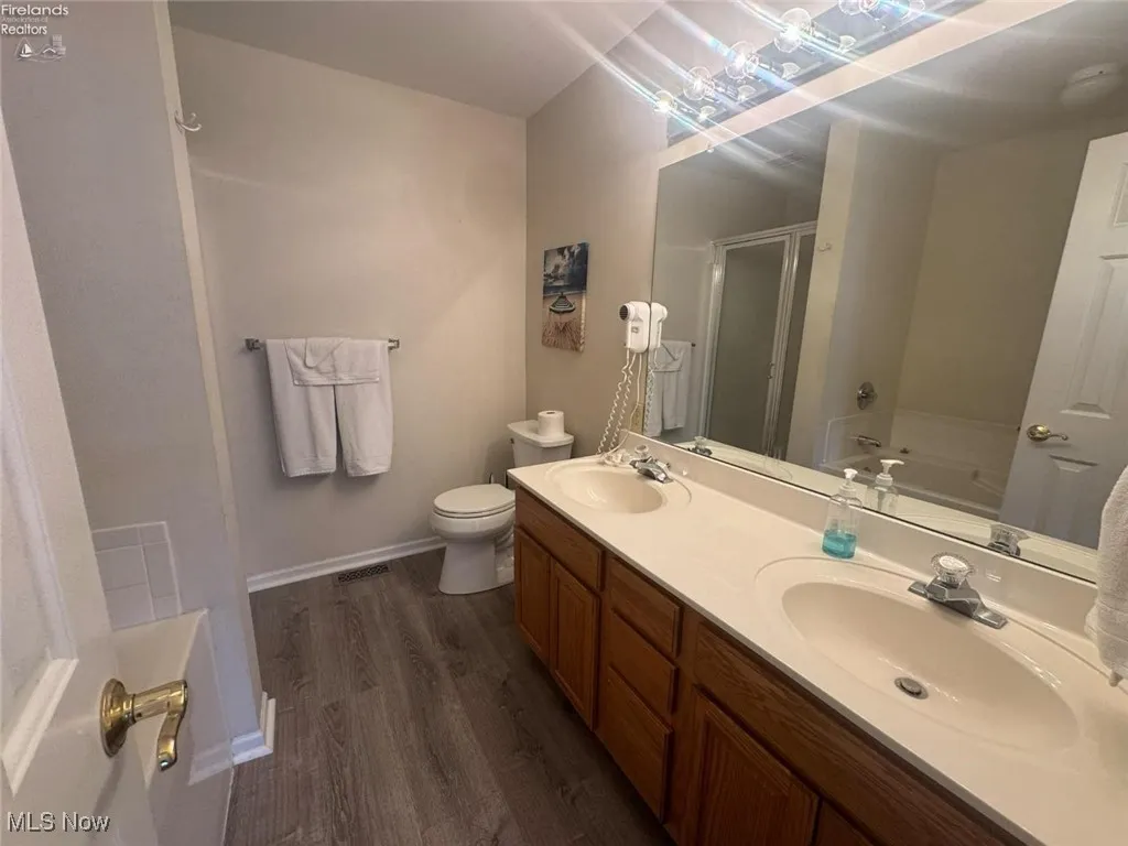 Bathroom with a stall shower, wood finished floors, a bath, double vanity, and toilet