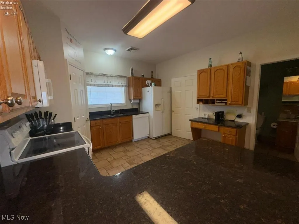 Kitchen featuring a sink, white appliances, brown cabinetry, and light flooring