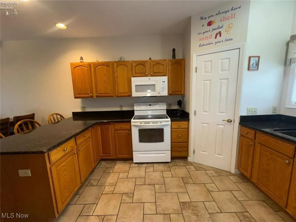 Kitchen with white appliances, brown cabinets, a peninsula, stone finish flooring, and recessed lighting