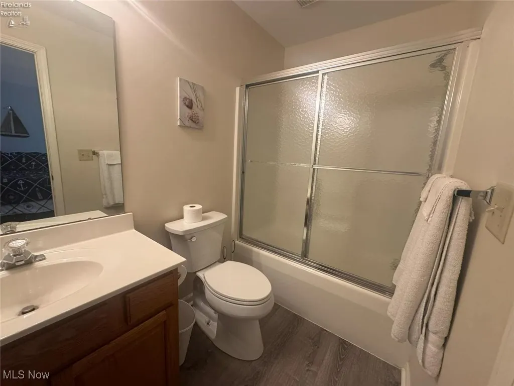 Bathroom with wood finished floors, vanity, toilet, and enclosed tub / shower combo