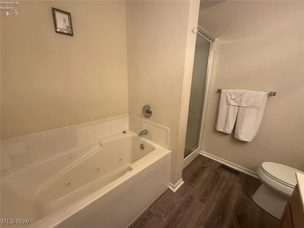 Bathroom with wood finished floors, a tub with jets, a shower stall, toilet, and baseboards