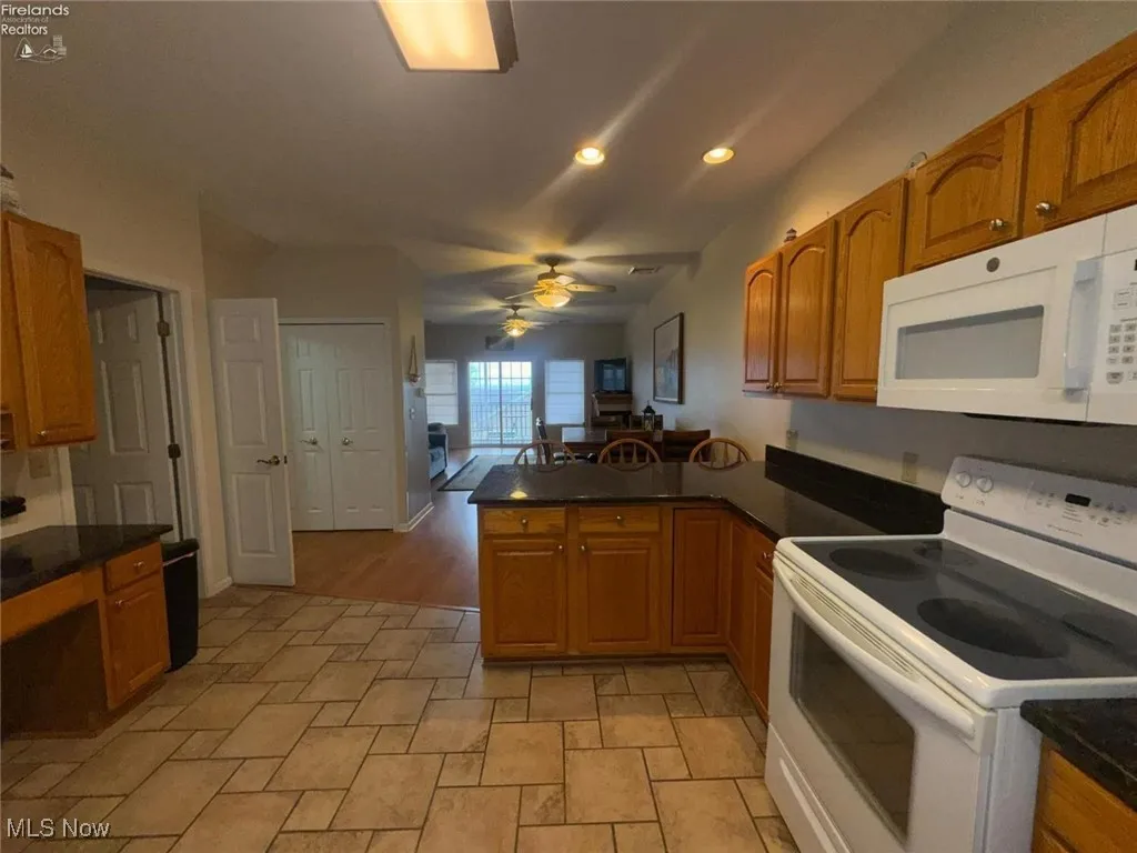 Kitchen featuring white appliances, a peninsula, dark countertops, a ceiling fan, and recessed lighting