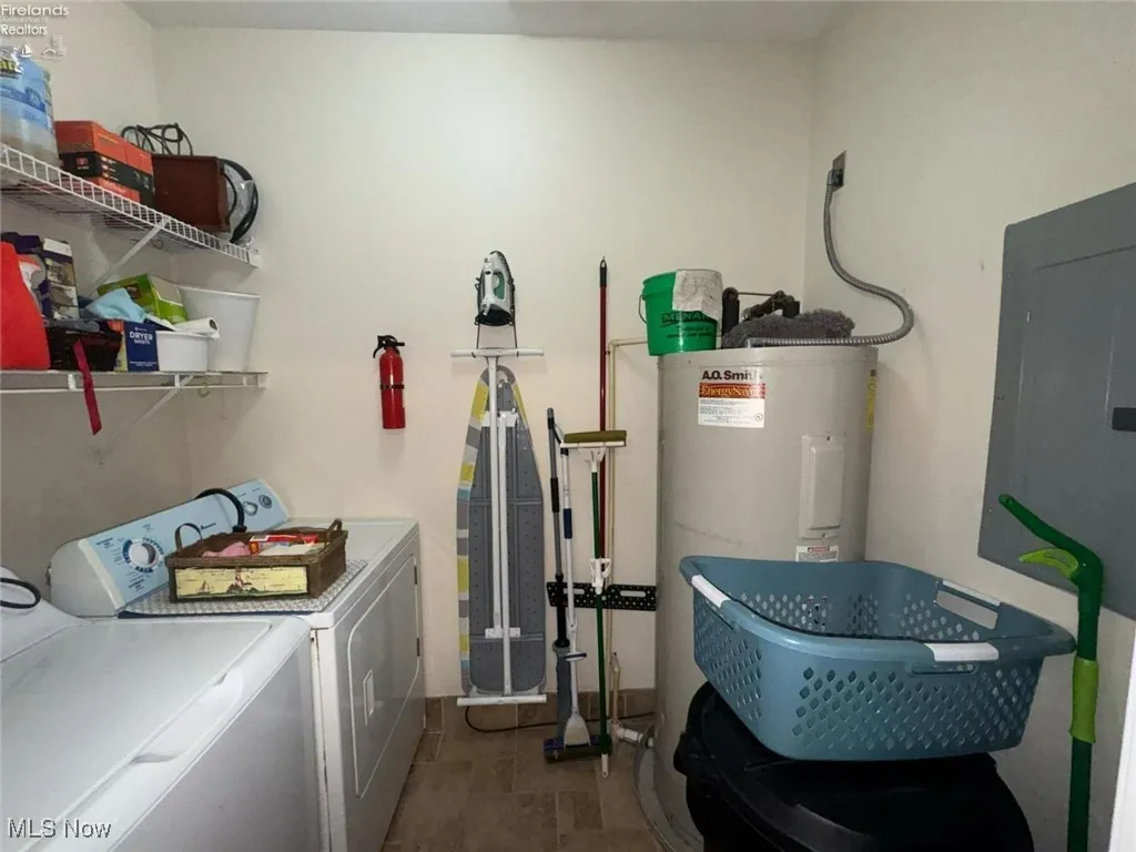 Clothes washing area featuring electric water heater, washer and clothes dryer, and electric panel
