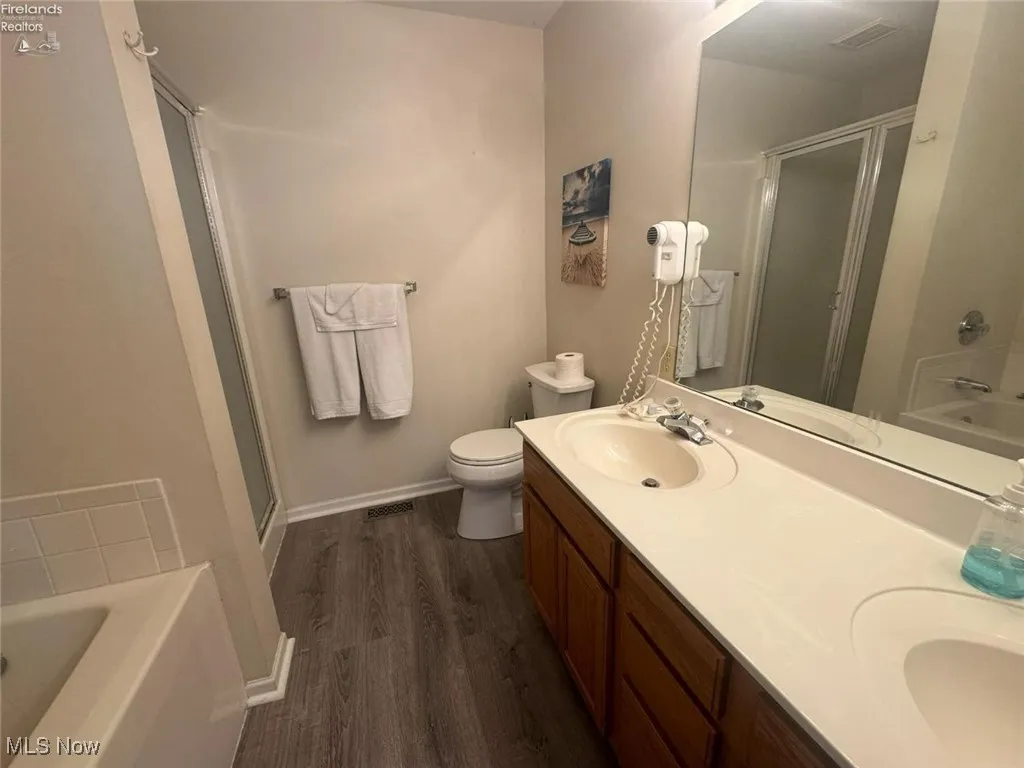 Bathroom with a shower stall, wood finished floors, a garden tub, and toilet
