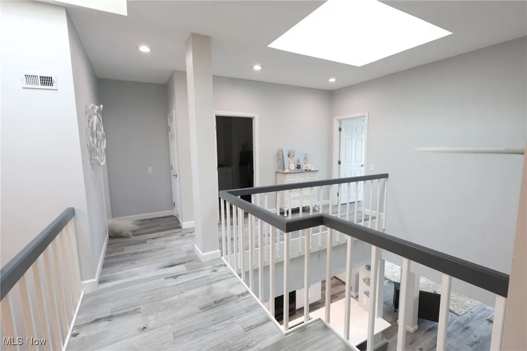 Corridor with an upstairs landing, a skylight, wood finished floors, recessed lighting, and baseboards