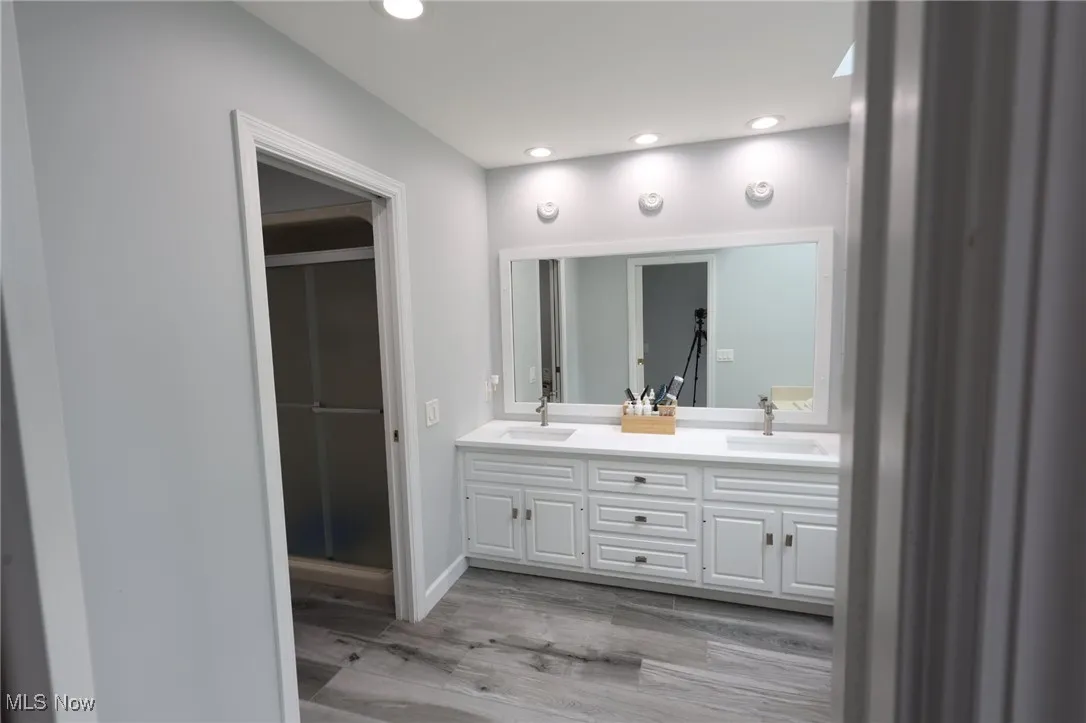 Bathroom featuring double vanity, wood finished floors, recessed lighting, baseboards, and a shower with shower door