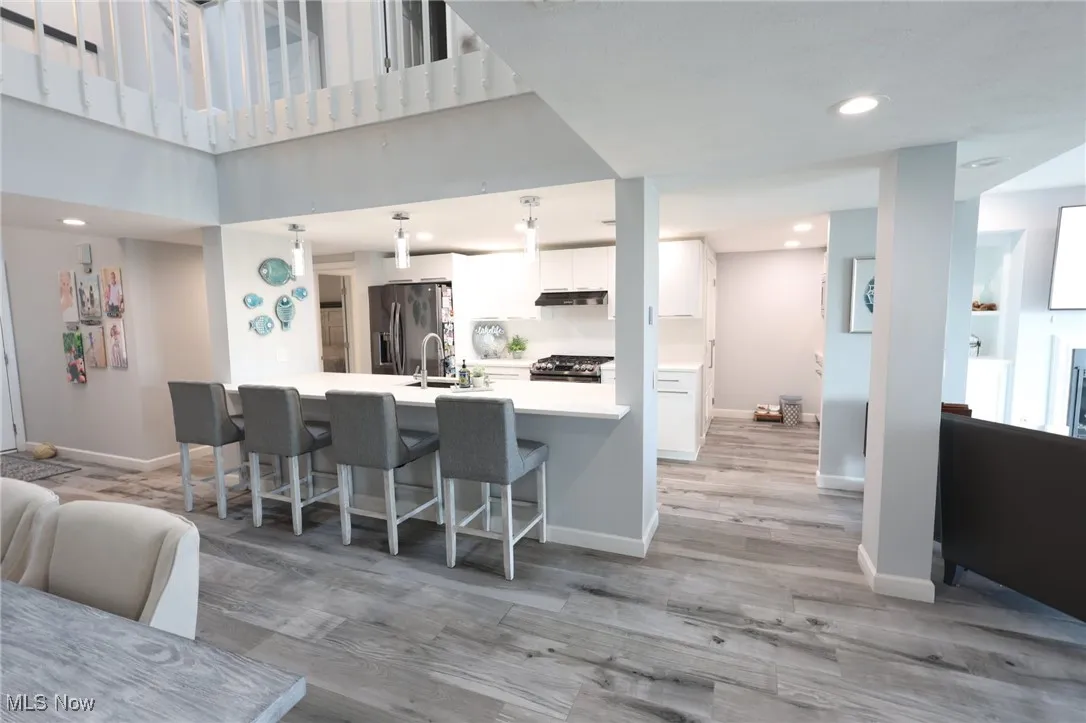 Kitchen with stainless steel fridge, white cabinetry, a kitchen bar, light countertops, and range