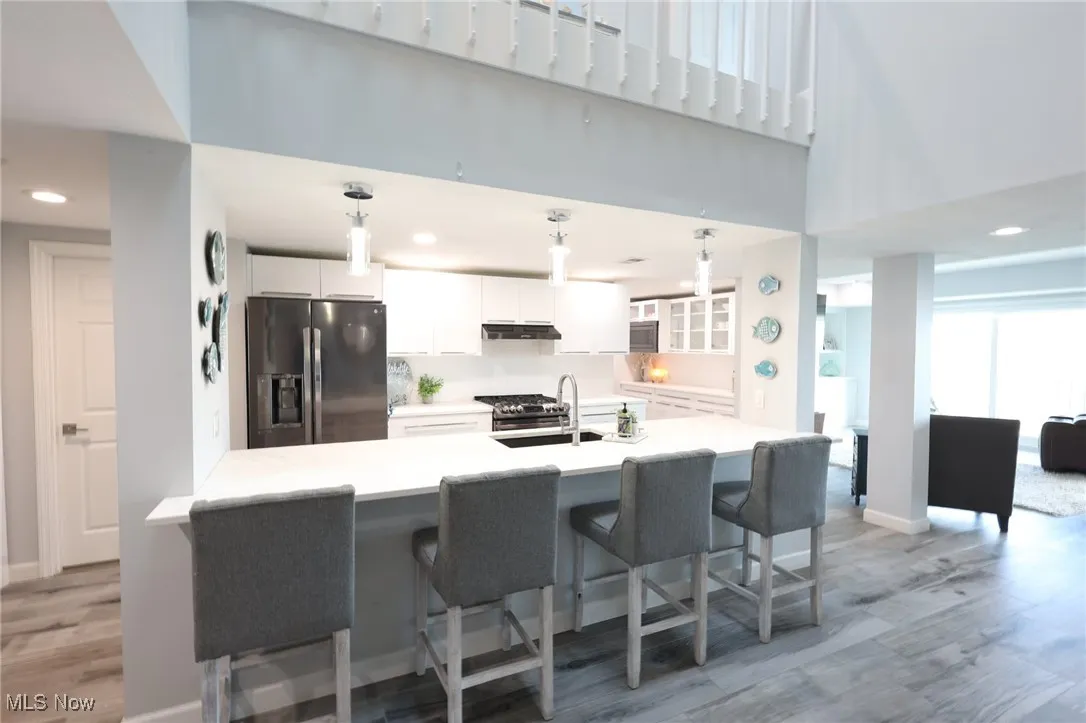 Kitchen featuring refrigerator with ice dispenser, under cabinet range hood, a sink, light wood-type flooring, and white cabinets