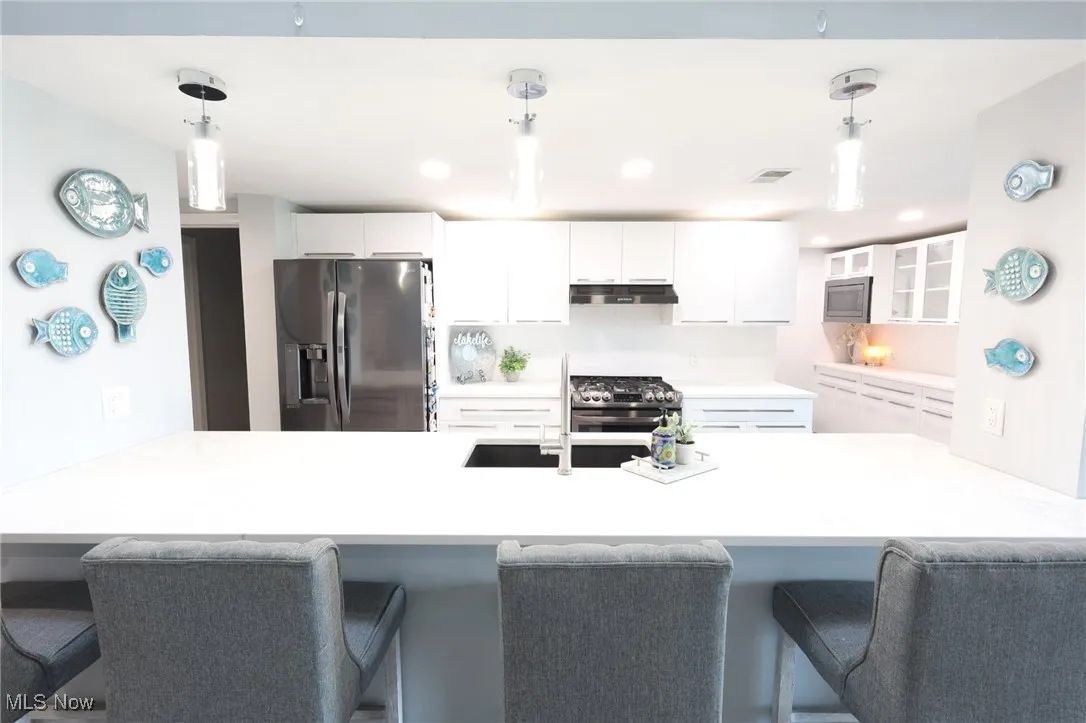 Kitchen with appliances with stainless steel finishes, under cabinet range hood, glass insert cabinets, and a peninsula