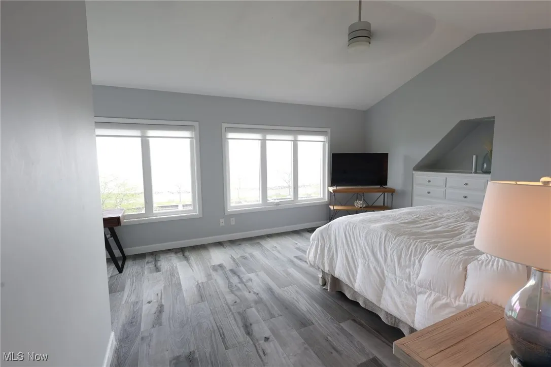 Bedroom with vaulted ceiling, wood finished floors, baseboards, and ceiling fan