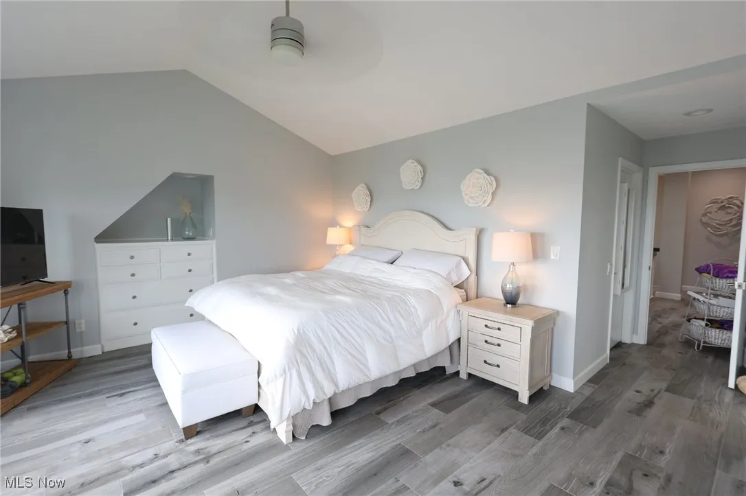 Bedroom with wood finished floors, vaulted ceiling, and baseboards