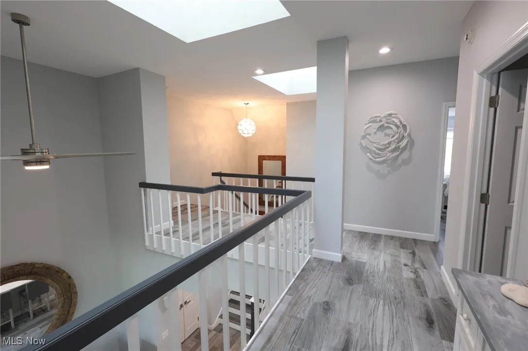 Hall with a skylight, an upstairs landing, wood finished floors, baseboards, and recessed lighting