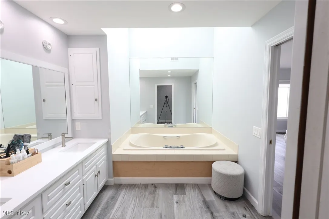 Bathroom with wood finished floors, a garden tub, double vanity, baseboards, and recessed lighting