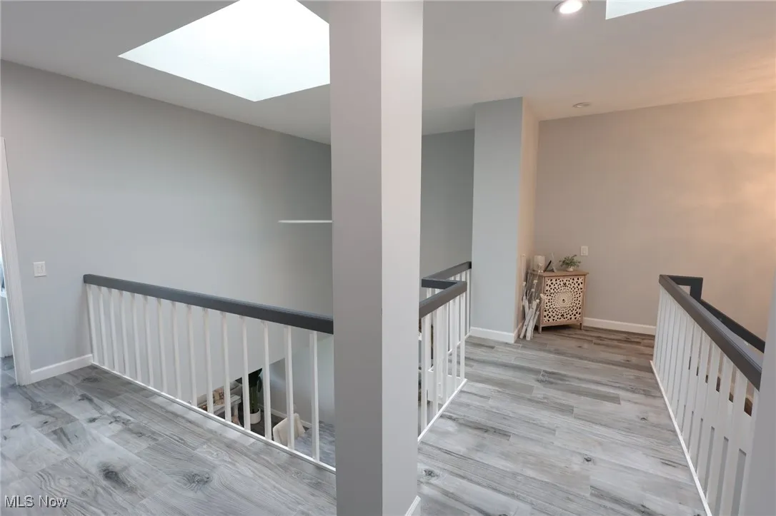Hall featuring an upstairs landing, a skylight, and wood finished floors