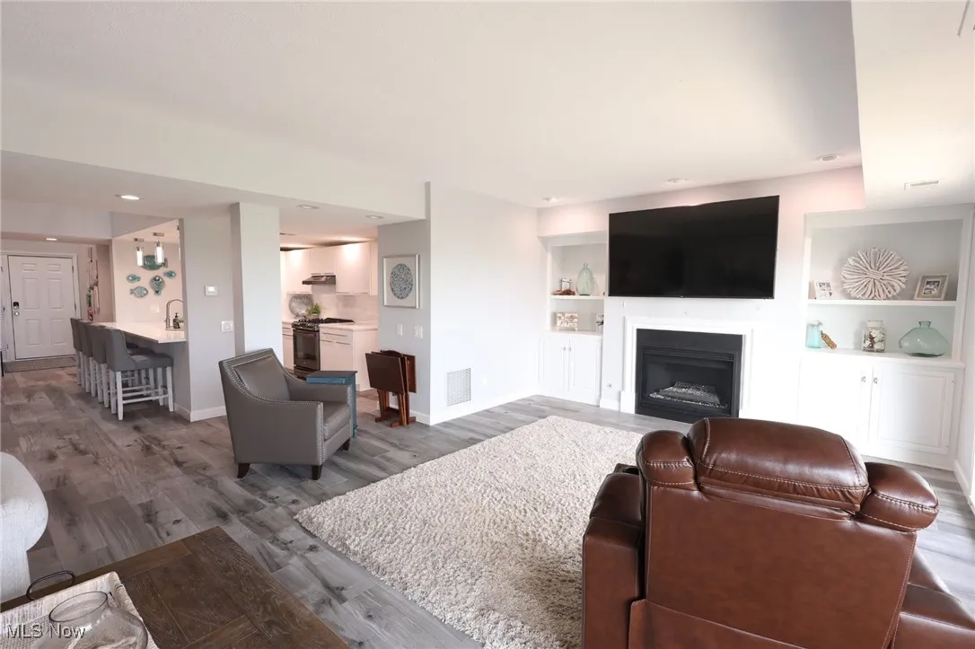 Living room featuring wood finished floors, baseboards, a fireplace, and built in features