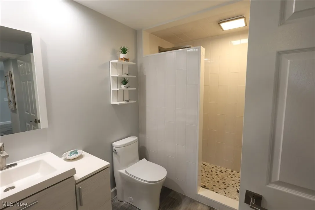 Bathroom featuring walk in shower, toilet, vanity, and wood finished floors