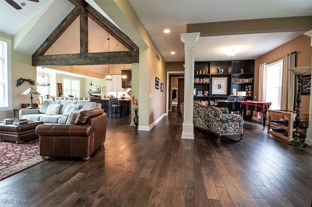 Virtually staged Living room featuring dark hardwood floors, built in features, high vaulted ceiling, and ornate columns