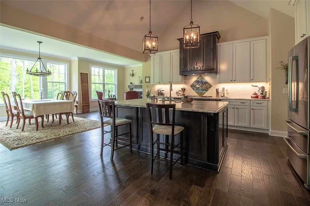Virtually staged Kitchen featuring lots of cabinets, quartz tiled counterstasteful backsplash, a large island island, a sink, dark hardwood  wood flooring, and hanging light fixtures