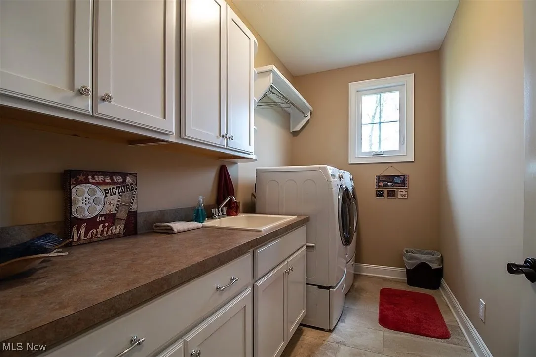 Virtually staged Laundry room with sink, washing machine and dryer, light tile flooring, and cabinets