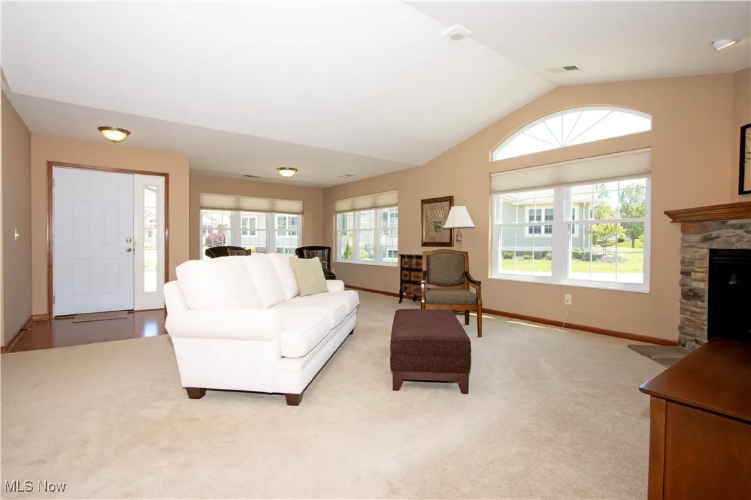 Living area featuring vaulted ceiling, light colored carpet, a stone fireplace, and baseboards