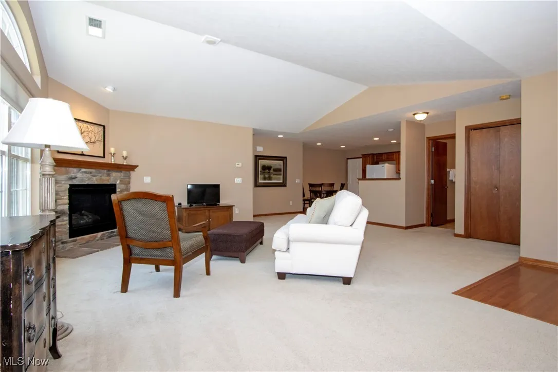 Living room with vaulted ceiling, a stone fireplace, light colored carpet, and baseboards